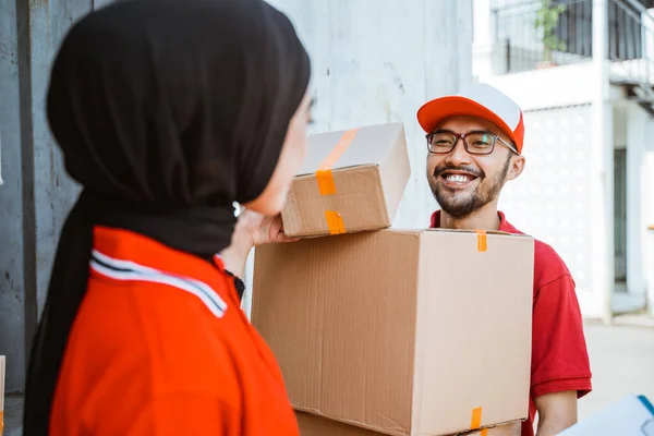 male workers assisted by women wearing hijabs lift packages from inside containers