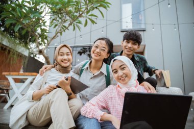 smiling young people working together on a laptop sitting against a building in the background