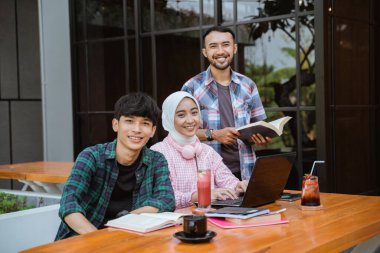 two male students and one female student smiling looking at the camera in a cafe