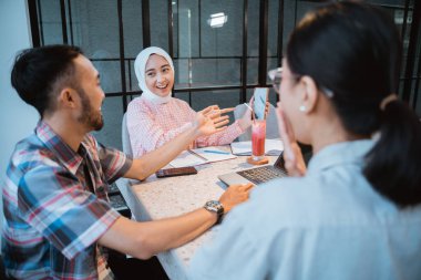 three college students chatting and looking at cellphone screens during group work together in a cafe