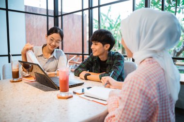 group of friends using a laptop and books during group work together in a cafe