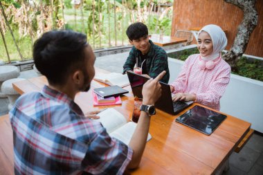 Asian students in hijabs chatting while using a laptop in a cafe