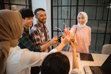 several young people toast with glasses as they gather in the cafe