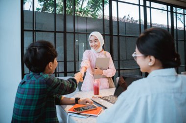 Asian student in hijab shaking hands with a boy when meeting in a cafe