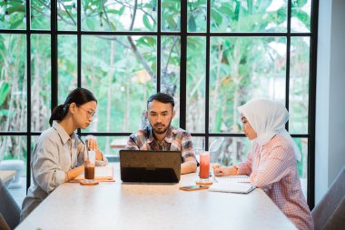 male college student and two female students using a laptop while doing assignments in a cafe in the background