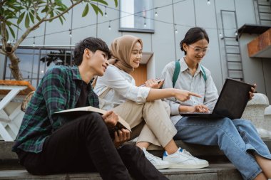 Three young asian college students using laptops sitting on steps in cafe