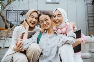 three asian student girls smiling while sitting together in cafe