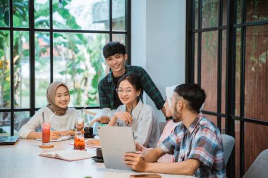 five young asian people doing homework together in cafe against glass window background