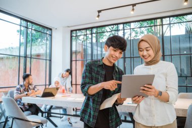 Asian student couple using a tablet with friends meeting in cafe as background