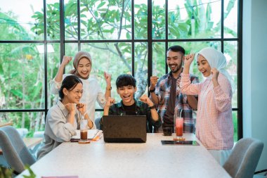 some young people are excited by the movement of their hands clenching when looking at a laptop in a cafe