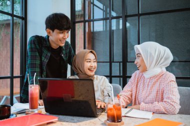 Young Asian people using a laptop and chatting in a cafe with glass windows in the background
