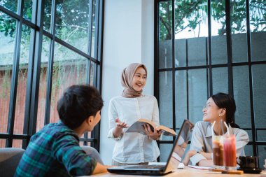 girl wearing a headscarf explains a problem to her friend while doing the assignment