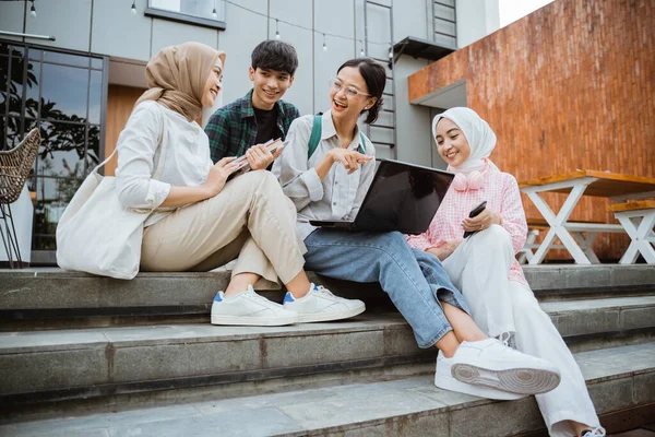 group of young college students using laptops sitting on the steps in a cafe