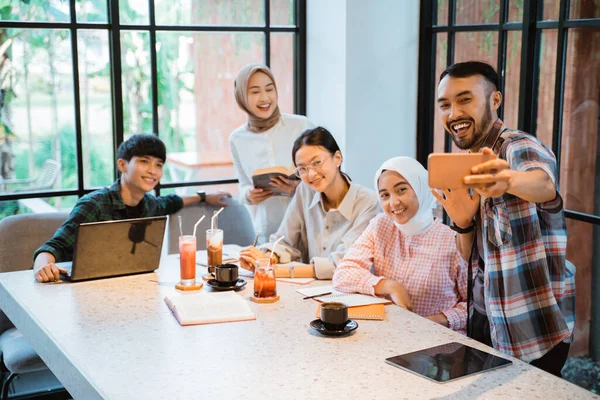 a group of young asian people smiling while taking selfie using cell phone in cafe