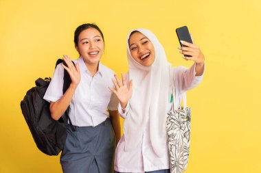 two high school girls waving during video call using handphone on isolated background