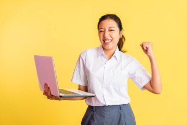 excited high school girl standing with fists clenched using a laptop on isolated background