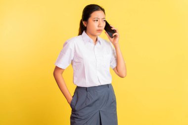 girl in high school uniform receiving phone call with smartphone on yellow background