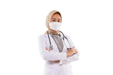 a beautiful doctor with hijab and mask on her face standing with the stethoscope at her shoulder and crossing her hands on the white background