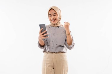 a beautiful woman with hijab standing and clenched her arm while looking at the phone at her hand on the white background