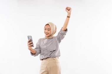 a beautiful woman with hijab raise and clenched her arm while standing looking at her phone on the white background