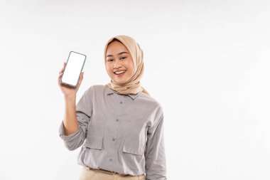 a beautiful woman with hijab standing with smile while raising and showing the phone at her hand with the white background