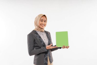a beautiful woman with hijab and gray blazzer standing with smile while showing and pointing on the tablet at her hand on the white background