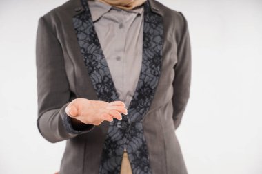 a beautiful woman with hijab and gray blazzer standing with one opened hand in front of her body on the white background