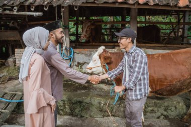 the moslem man hand shake with the male farmer while the male farmer holding the cows bridle at his left hand