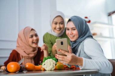 tesettürlü üç arkadaş telefona bakıyor ve yeni yemek tarifi arıyor.