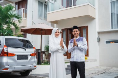 Muslim husband and wife with greeting hand gestures. Concept of Eid celebration at home