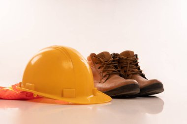 a leather boots beside the yellow hardhat and orange safety waistcoat on isolated background