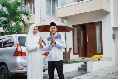 Asian husband and wife with greeting hand gestures. Concept of Eid celebration at home