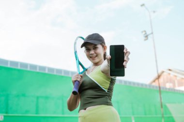 bottom view of female tennis player holding racket showing mobile phone screen on tennis court