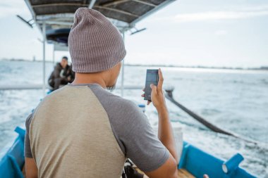 seen from behind fisherman using cellphone on small fishing boat