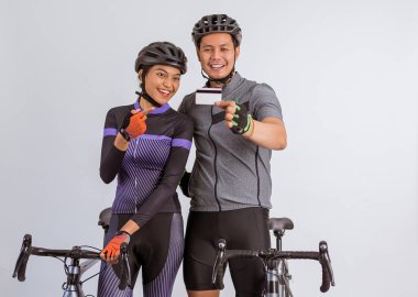asian couple in cycling outfit showing the blank card while standing beside their bicycles on isolated background