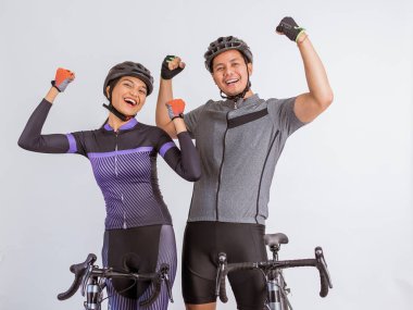 asian couple in cycling outfit raising their clenched arms while standing beside their bicycles on isolated background