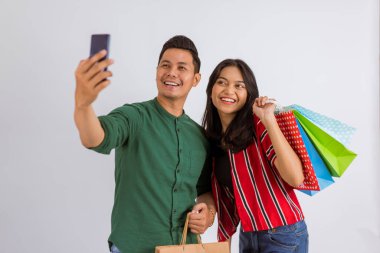 asian couple taking groufie photo while holding the shopping bags on isolated background