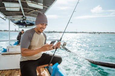 fisherman using a smartphone to send messages while fishing at sea on a small fishing boat