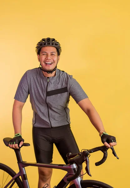 asian man in sporty outfit smiling while standing beside his bicycle on isolated background