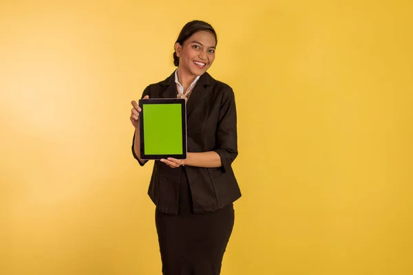 asian woman in formal outfit showing the digital tablet with green screen on orange isolated background