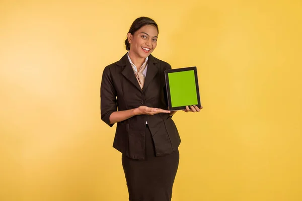 asian woman in formal outfit showing and pointing on the digital tablet with green screen on orange isolated background