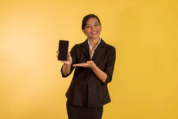 asian woman in formal outfit standing with smile and showing the phone on orange isolated background