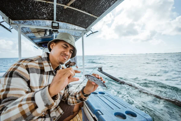 sad angler gets a small fish while fishing at sea using a small fishing boat