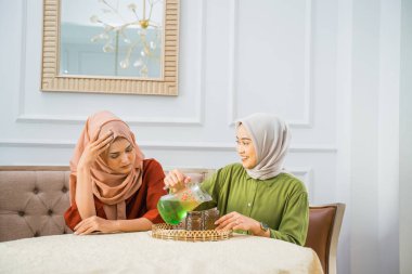 Asian woman in hijab serves drinks when her sad friend visits home