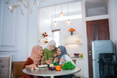 three friend with hijab looking at the phone searching for new recipe for dinner