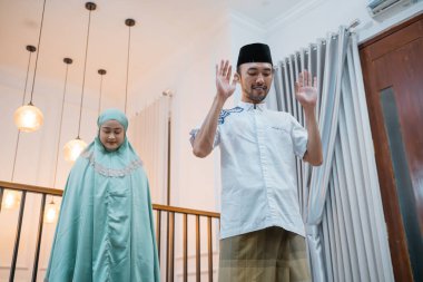 Asian Muslim man leads prayers with woman during Takbirotul Ihram movement during prayers at home