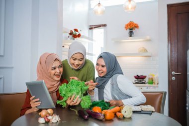 three friend with hijab looking tablet and learn to make new food menu in the kitchen. cooking recipe