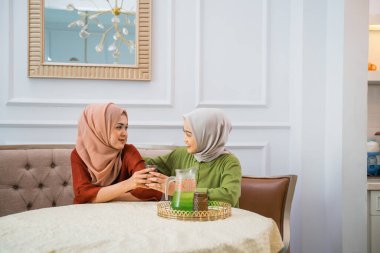 Asian woman in hijab serves drinks while chatting with her friend at home