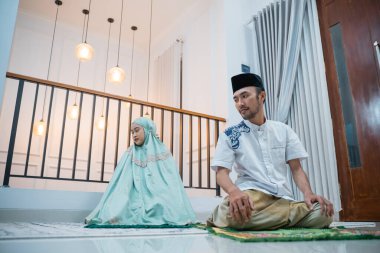 husband leads prayer with wife while sitting saying assalamualaikum warahmatullah wabarakatuh when praying on a prayer mat at home