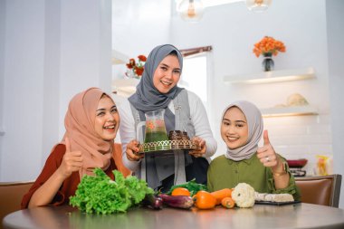 happy friend serving fresh drink for her friend at the kitchen during cooking for dinner